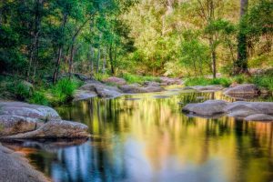 A peaceful scene of a still river with rocks and trees.
